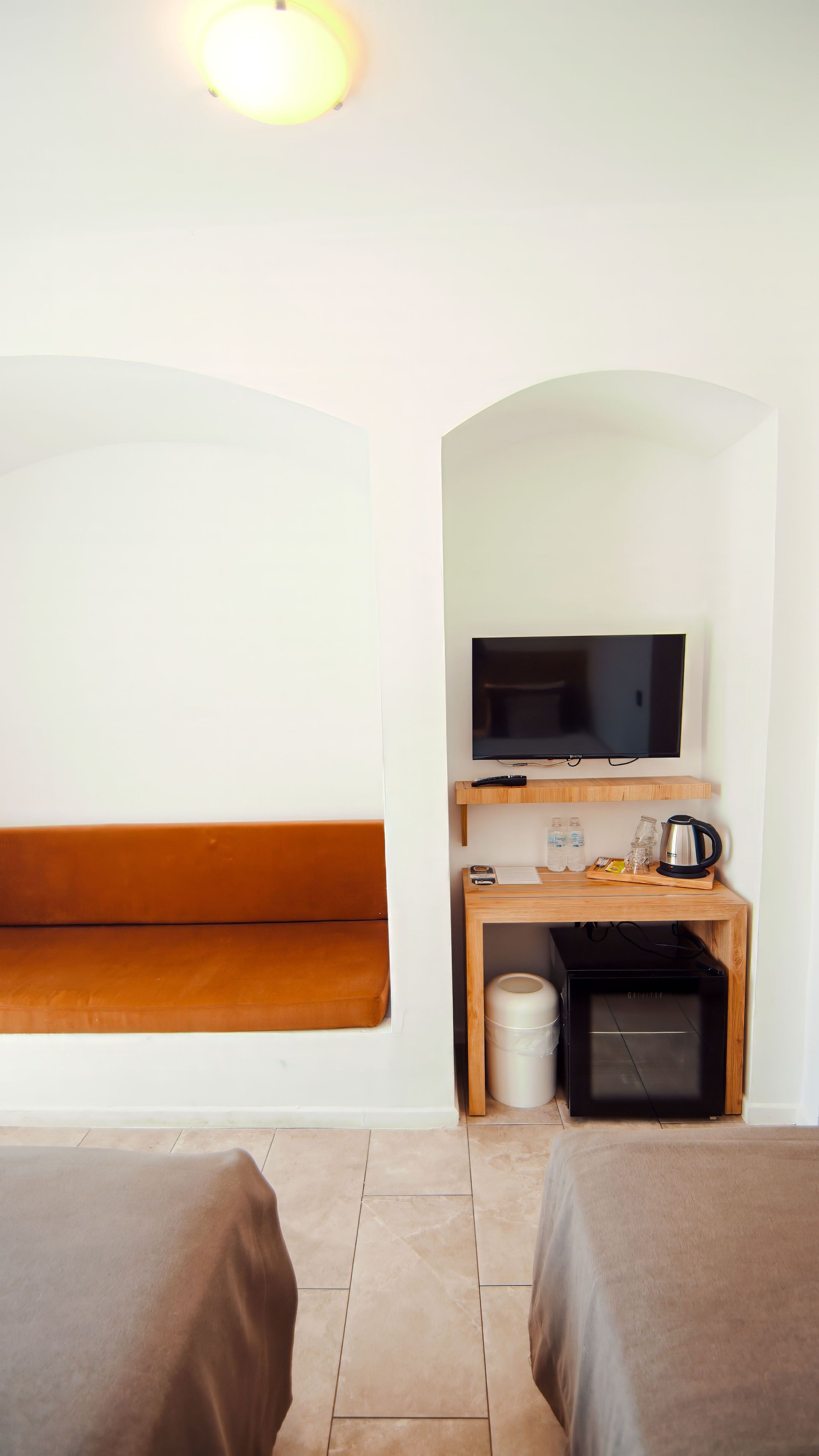 A room with two beds, a TV, a wooden table with a kettle, and a trash bin.