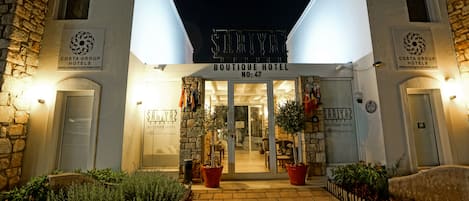 A boutique hotel entrance with a stone facade, potted plants, and a sign indicating it is part of the Costa Group Hotels.
