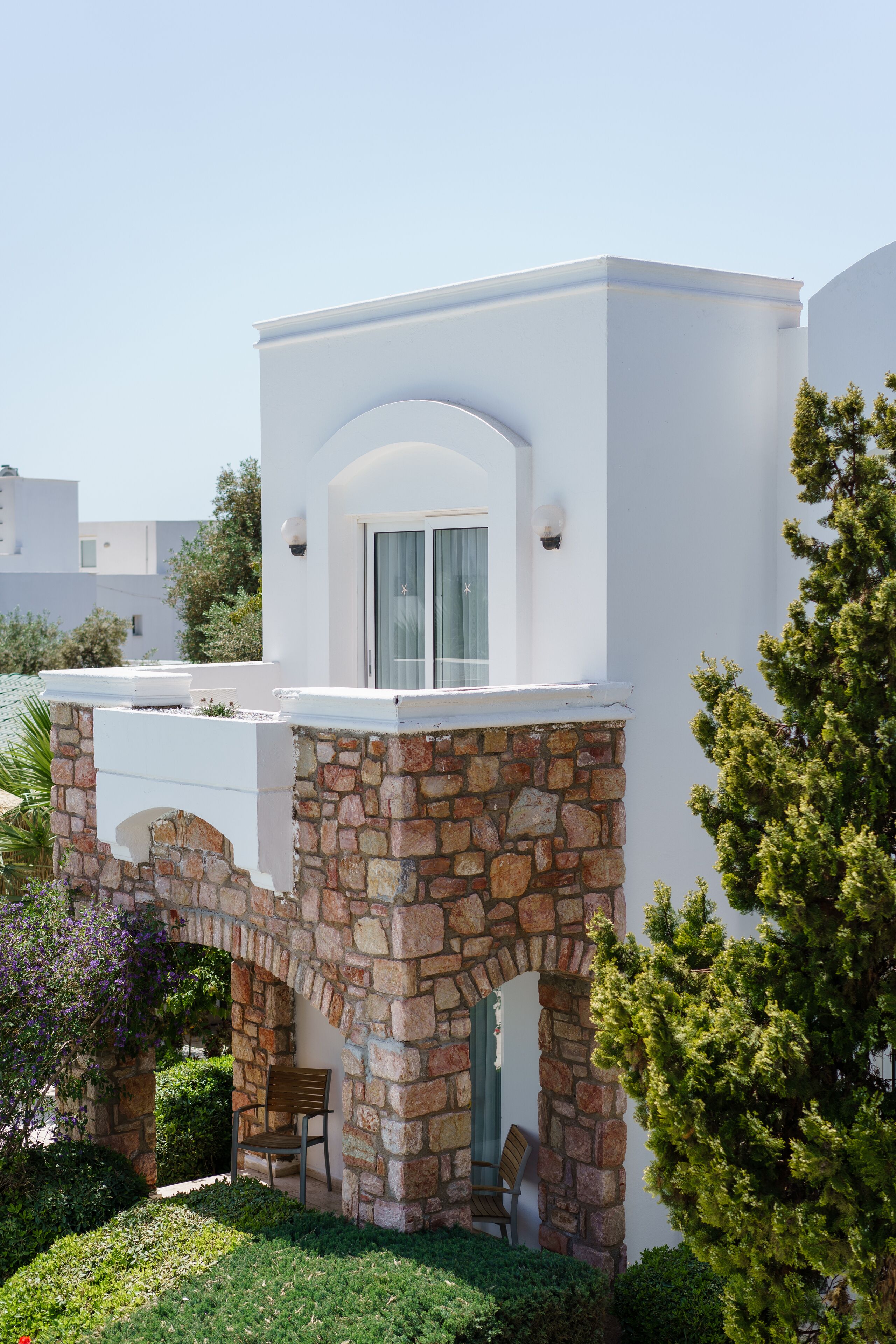 Un edificio moderno con un arco de piedra que conduce a una zona cubierta con dos sillas.