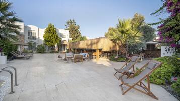 A courtyard with lounge chairs, a thatched-roof structure, and a sign reading "SABU".
