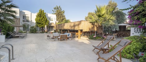 A courtyard with lounge chairs, a thatched-roof structure, and a sign reading "SABU".