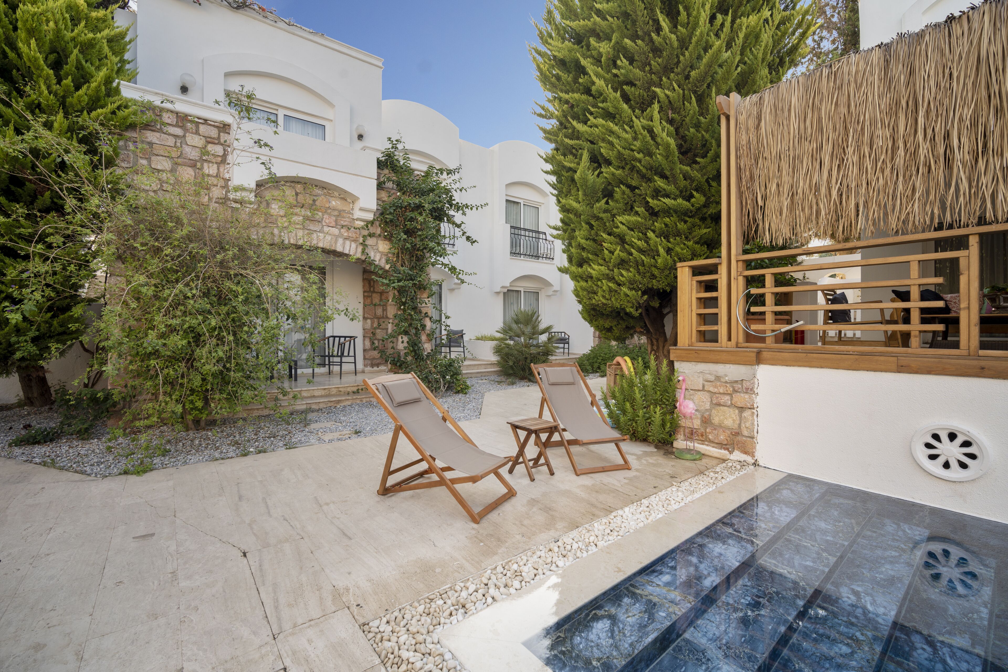 Un espace piscine avec des chaises longues, un mur en pierre et un bâtiment doté de balcons.