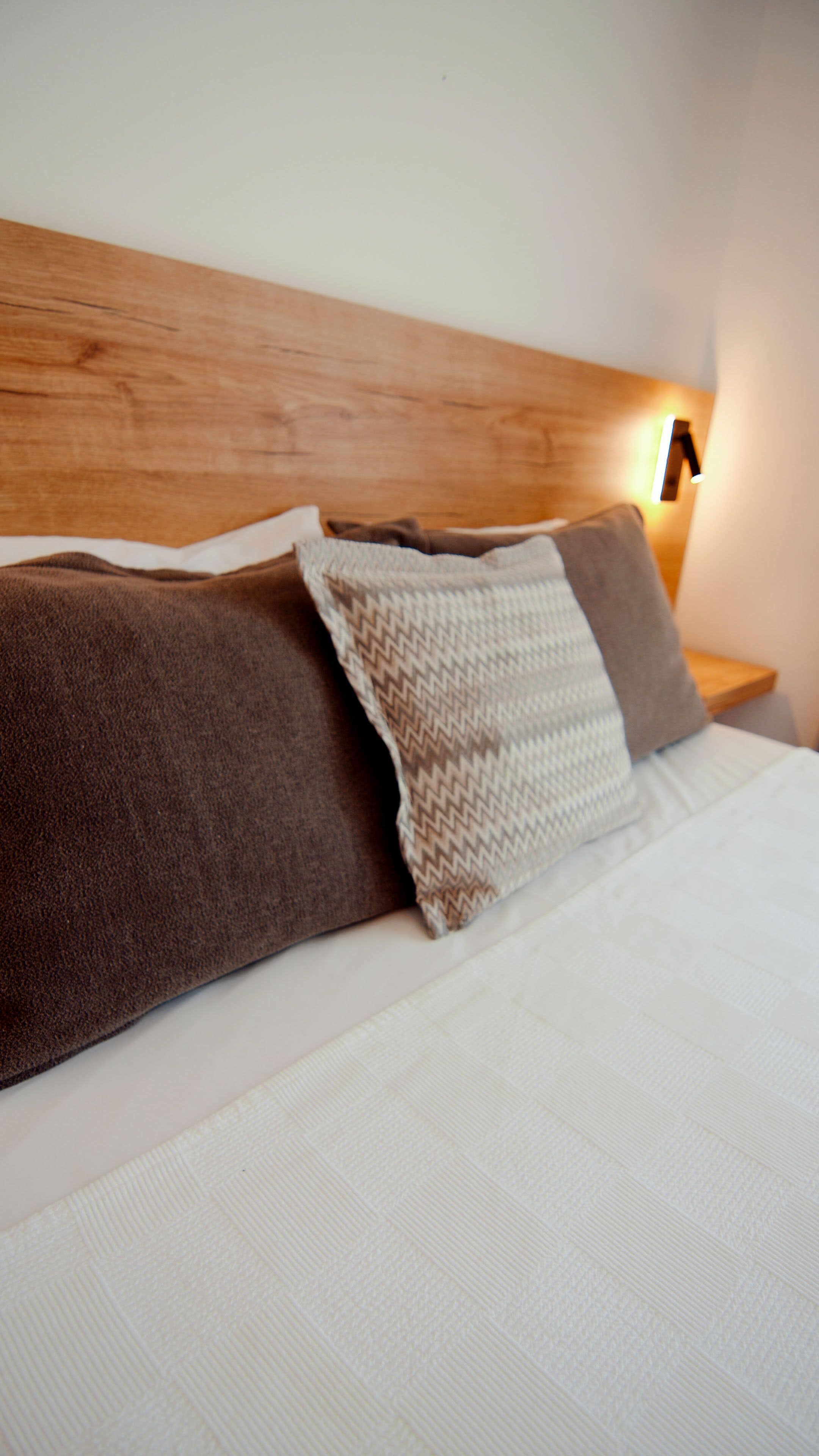 A bed with a wooden headboard, two pillows, and a bedside lamp.