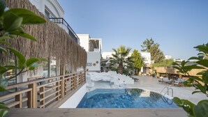 A pool area with a wooden deck, a thatched wall, and lounge chairs. - Costa Sariyaz Hotel (Bodrum)
