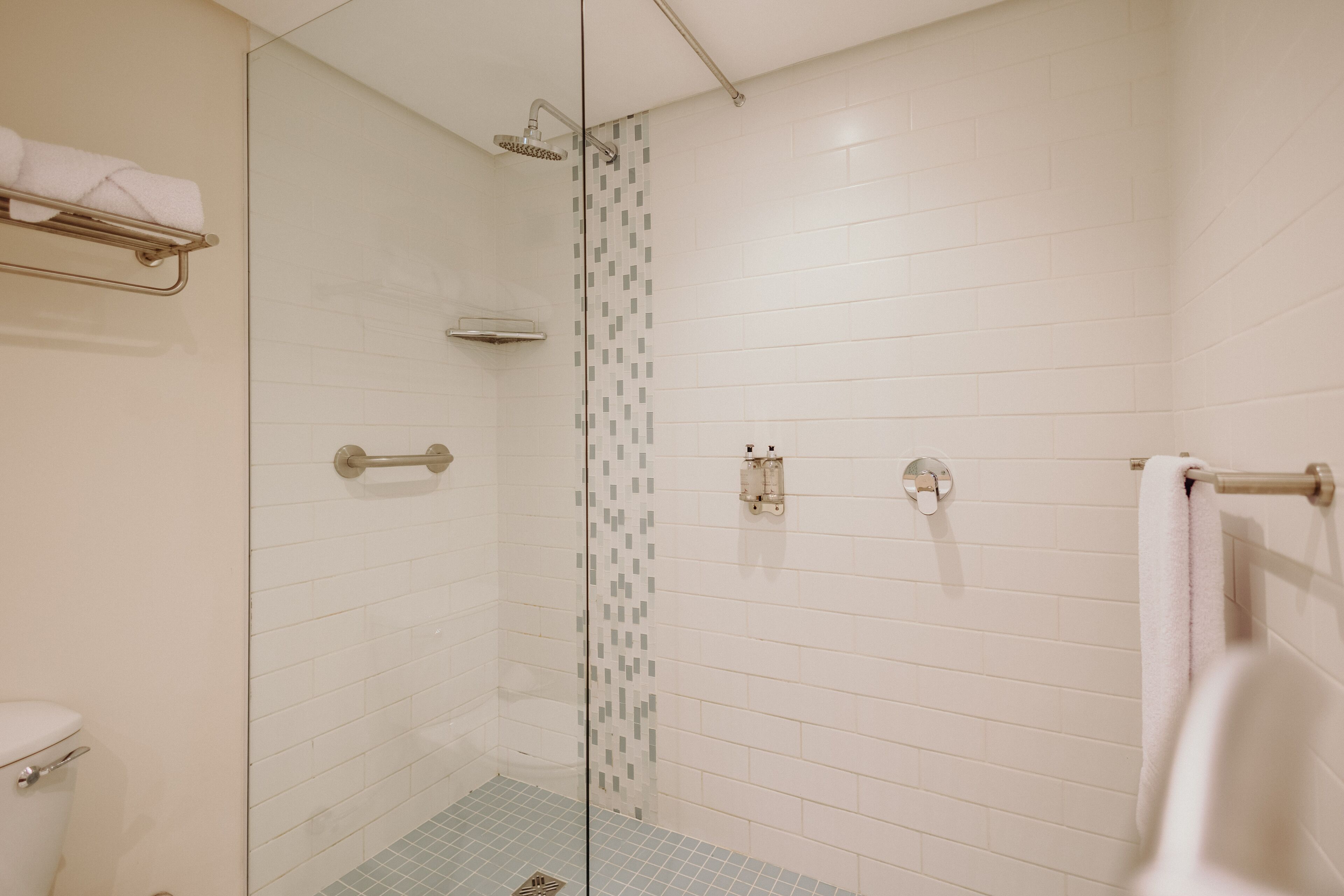 A modern bathroom with a glass shower enclosure, white tiled walls, and a blue-tiled floor.