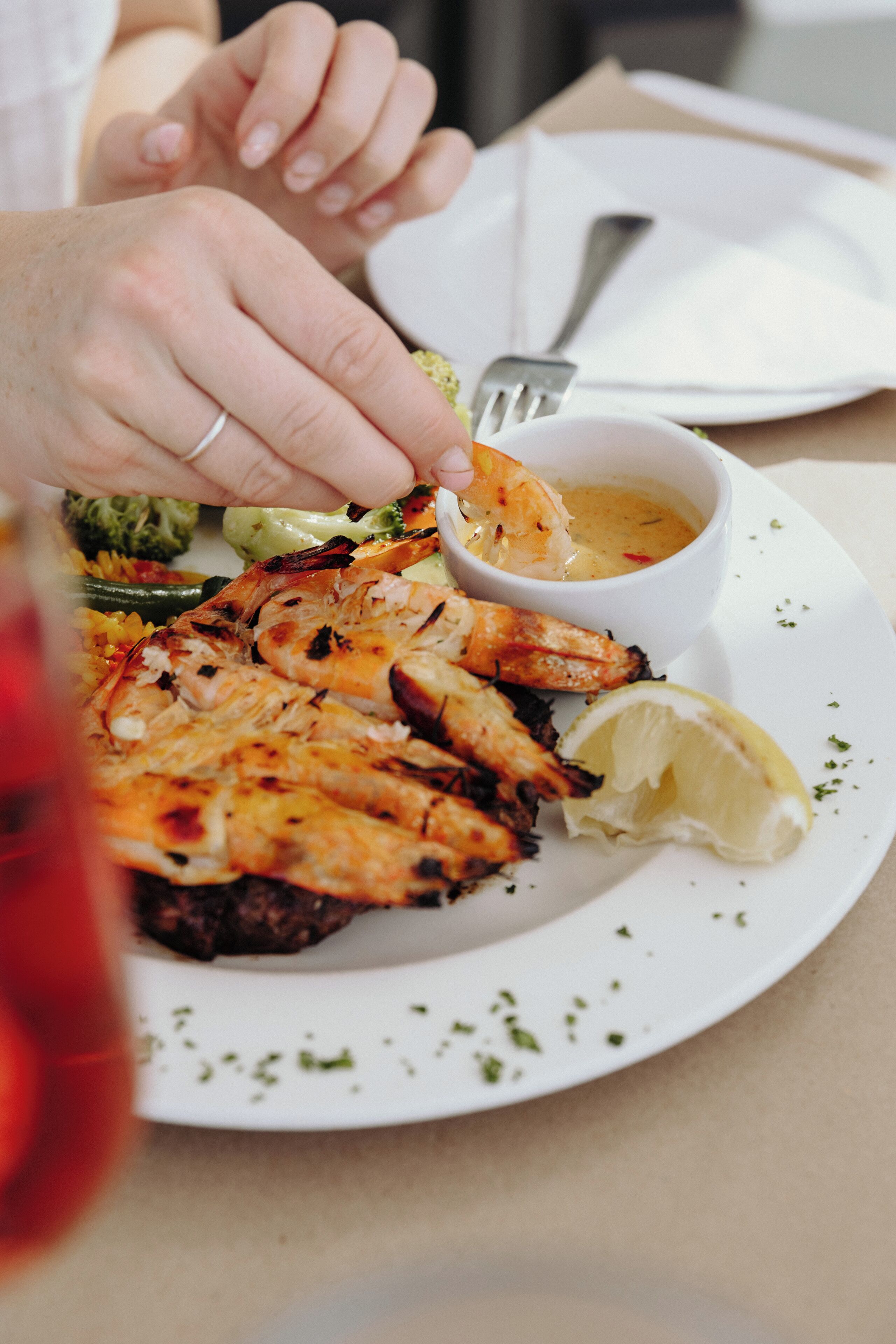A plate of grilled shrimp with lemon and a small bowl of sauce.