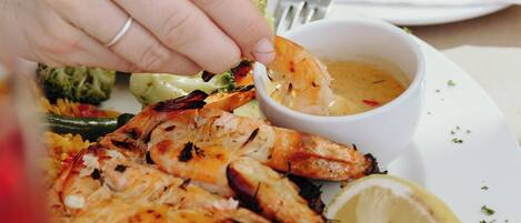 A plate of grilled shrimp with lemon and a small bowl of sauce.