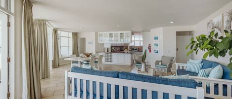 A spacious living area with a white sofa, a dining table, and a kitchen in the background.