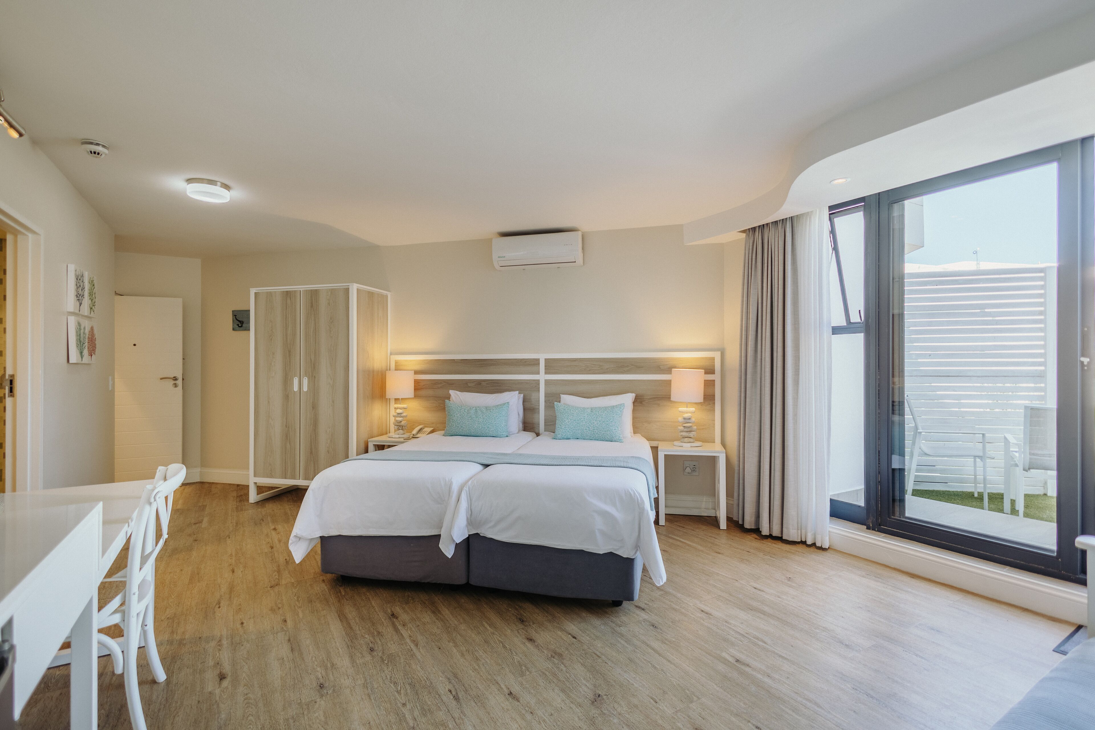 A modern hotel room with a double bed, a desk, and a large window with a view of the outdoors.