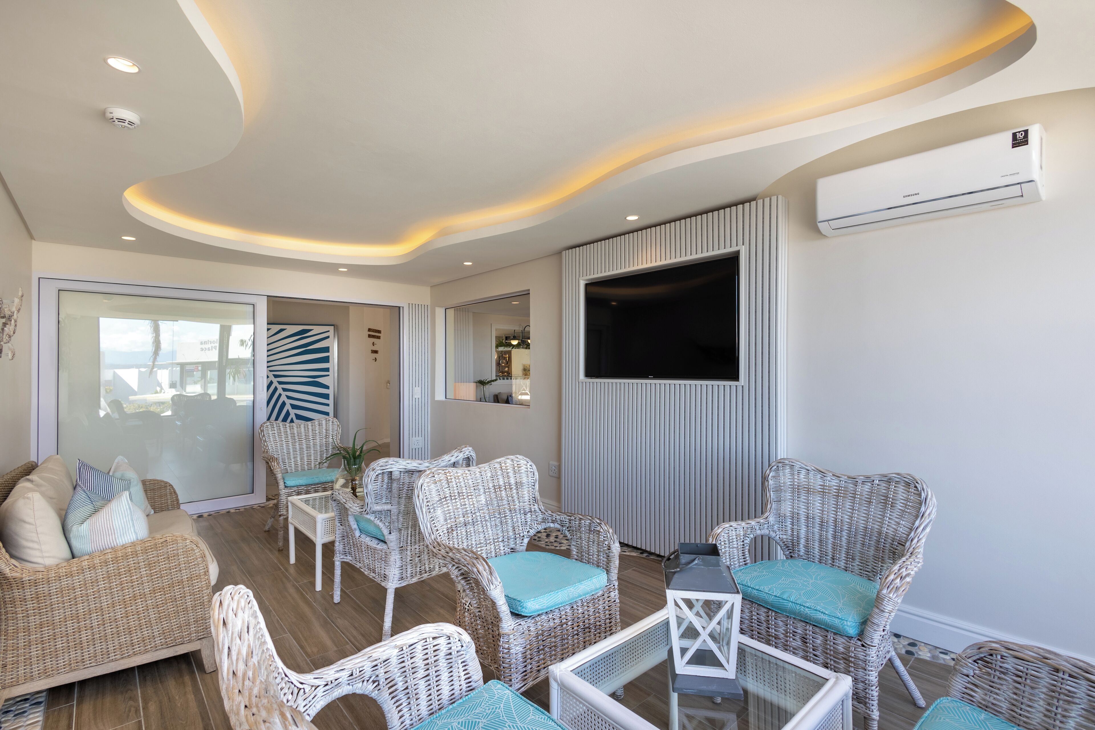 A modern living room with wicker furniture, a flat-screen TV, and an air conditioning unit.