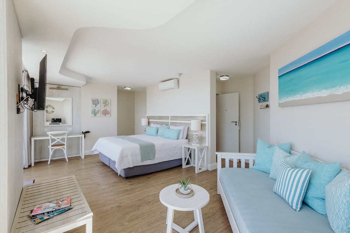 A modern bedroom with a bed, a desk, a chair, a small table, and a sofa.