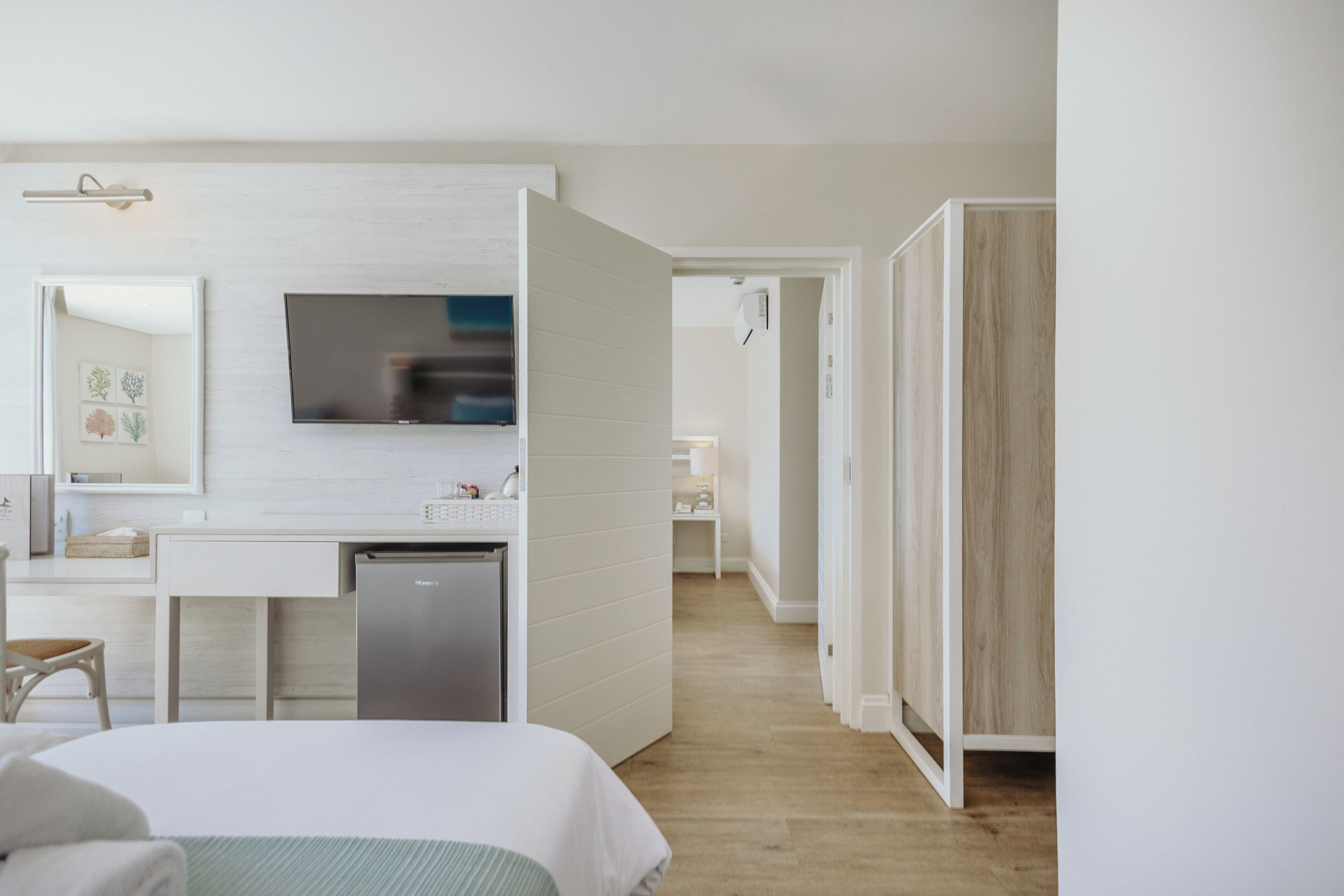 Una moderna camera d'hotel con un letto, una scrivania con televisore a schermo piatto, un minibar e un bagno con porta in legno.