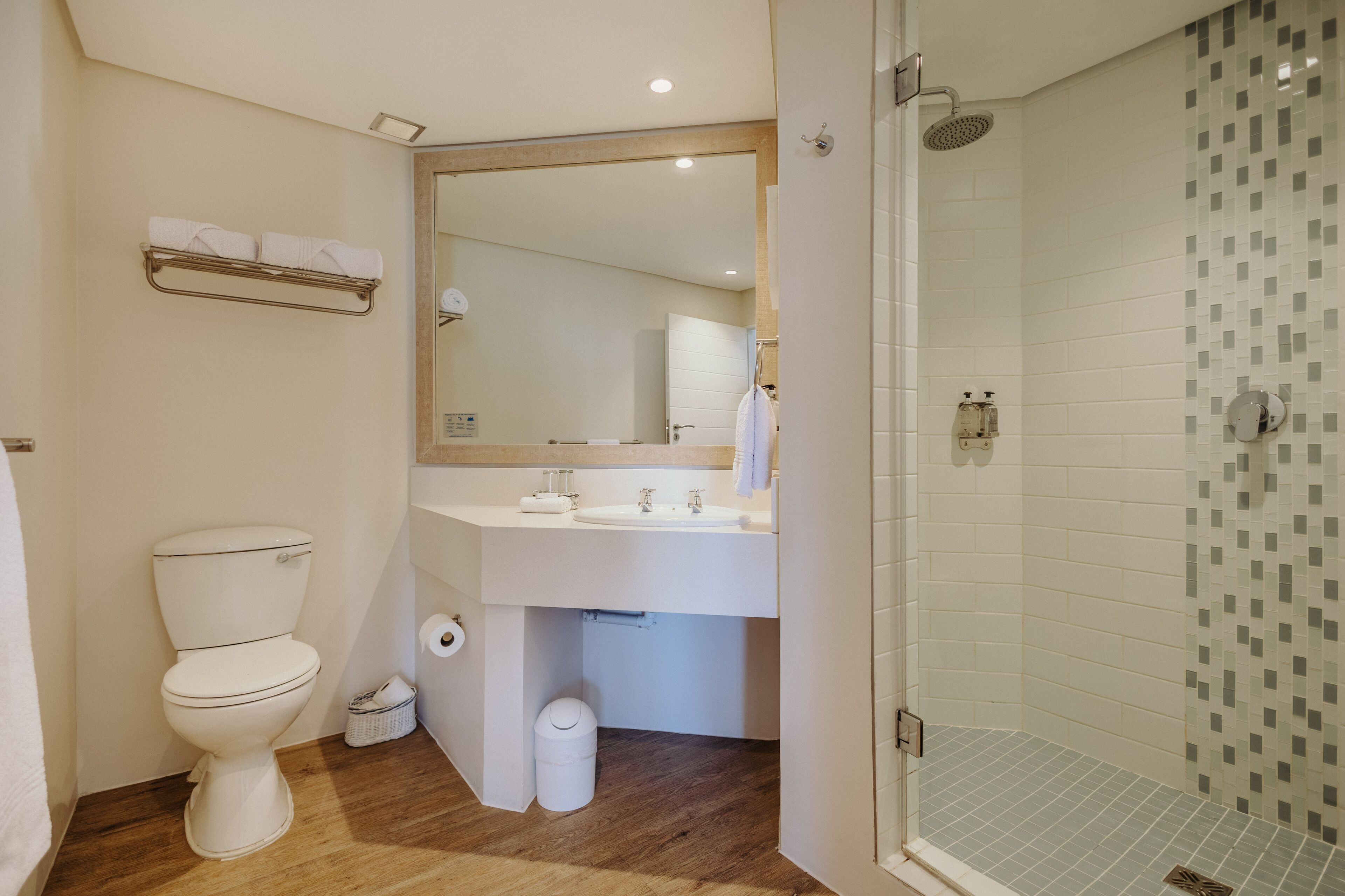 A modern bathroom with a toilet, sink, mirror, and shower.