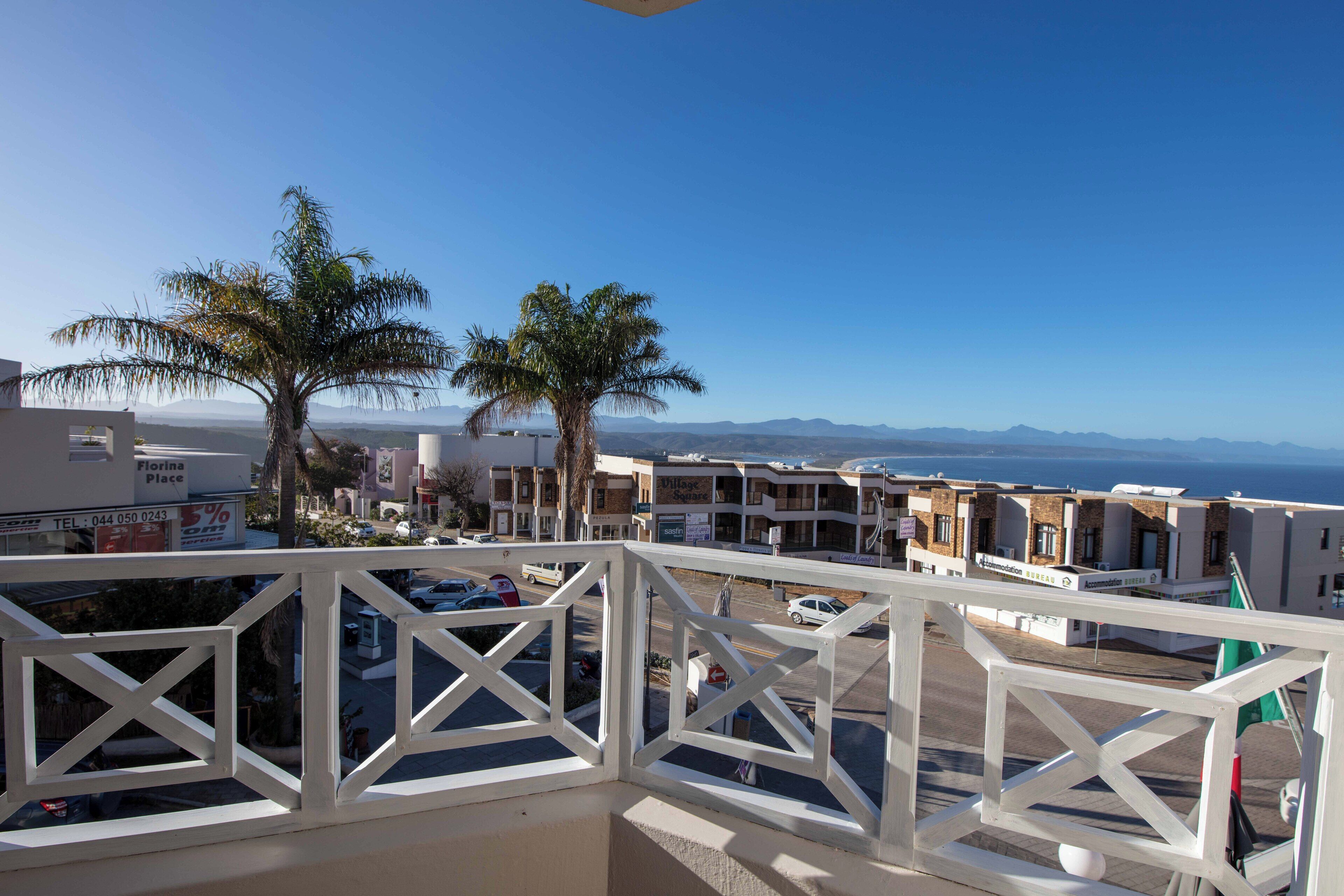 A balcony with a view of a coastal town, palm trees, and a clear sky.