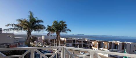 A balcony with a view of a coastal town, palm trees, and a clear sky.