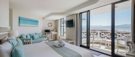 A modern hotel room with a large bed, a TV, and a balcony with outdoor seating.
