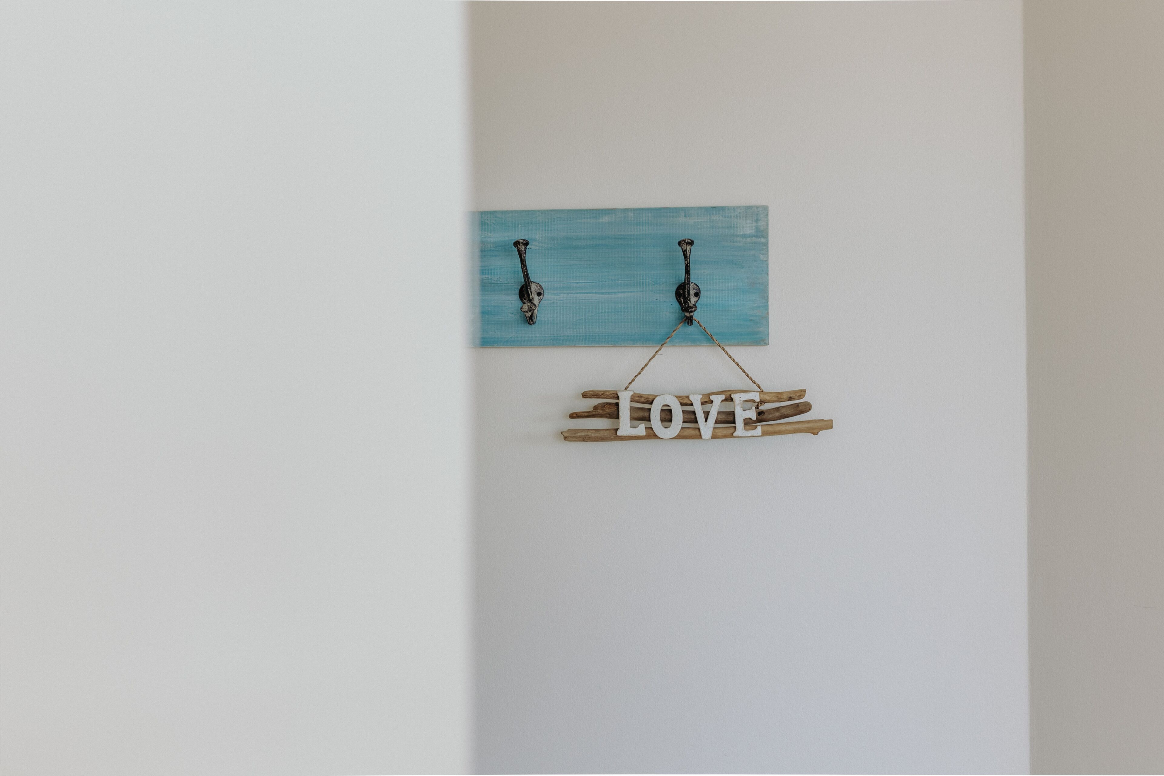 A wall-mounted decoration with a blue plaque and wooden letters spelling "LOVE" suspended by a rope.