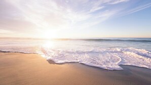 Une plage avec des vagues, un ciel dégagé et un coucher de soleil.