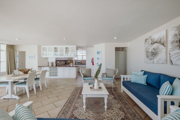 A spacious living area with a sofa, chairs, a dining table, and a kitchen in the background. - Bayview Hotel (Plettenberg Bay)