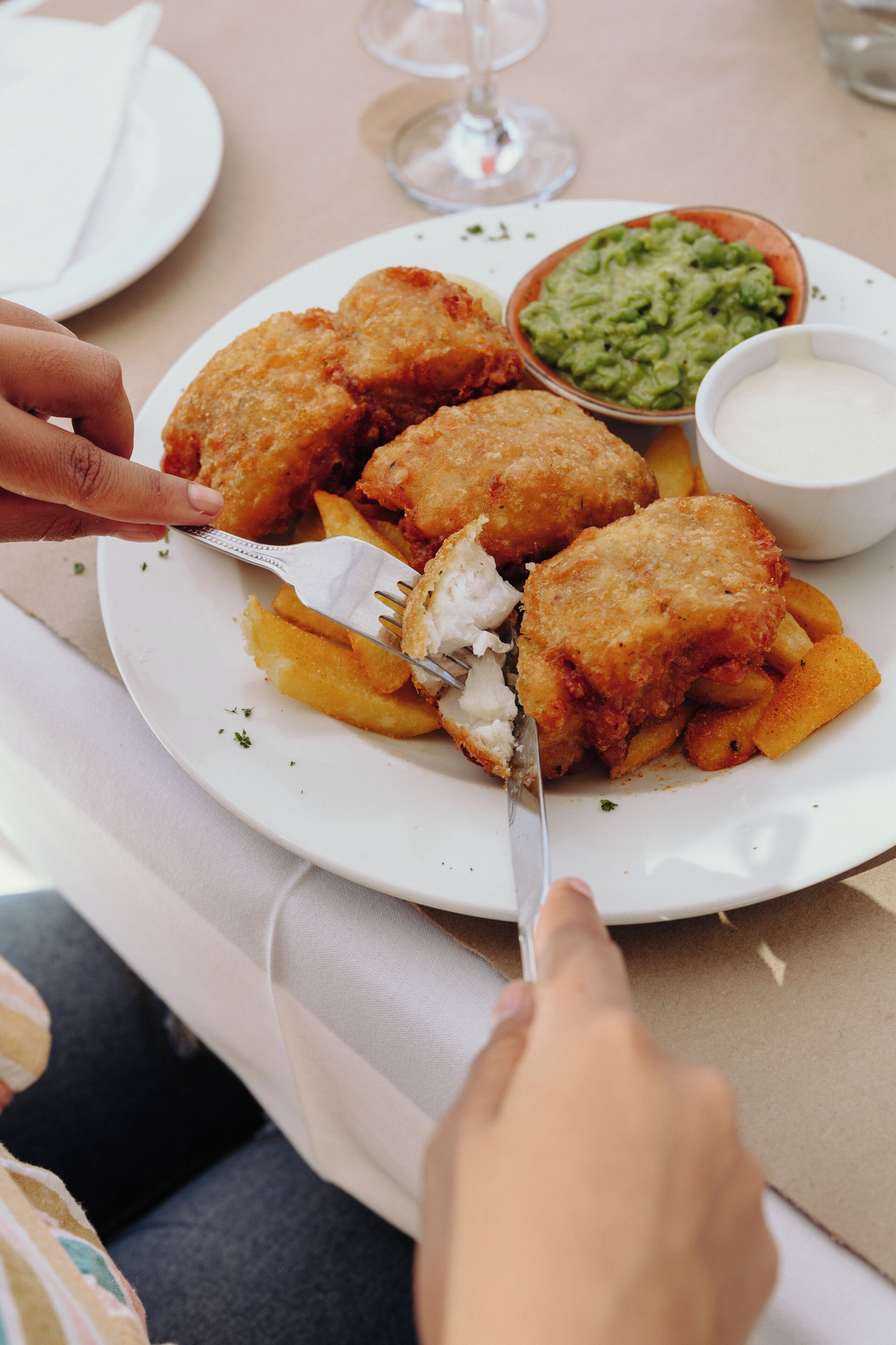 A plate of breaded fish fillets with fries and a side of guacamole.