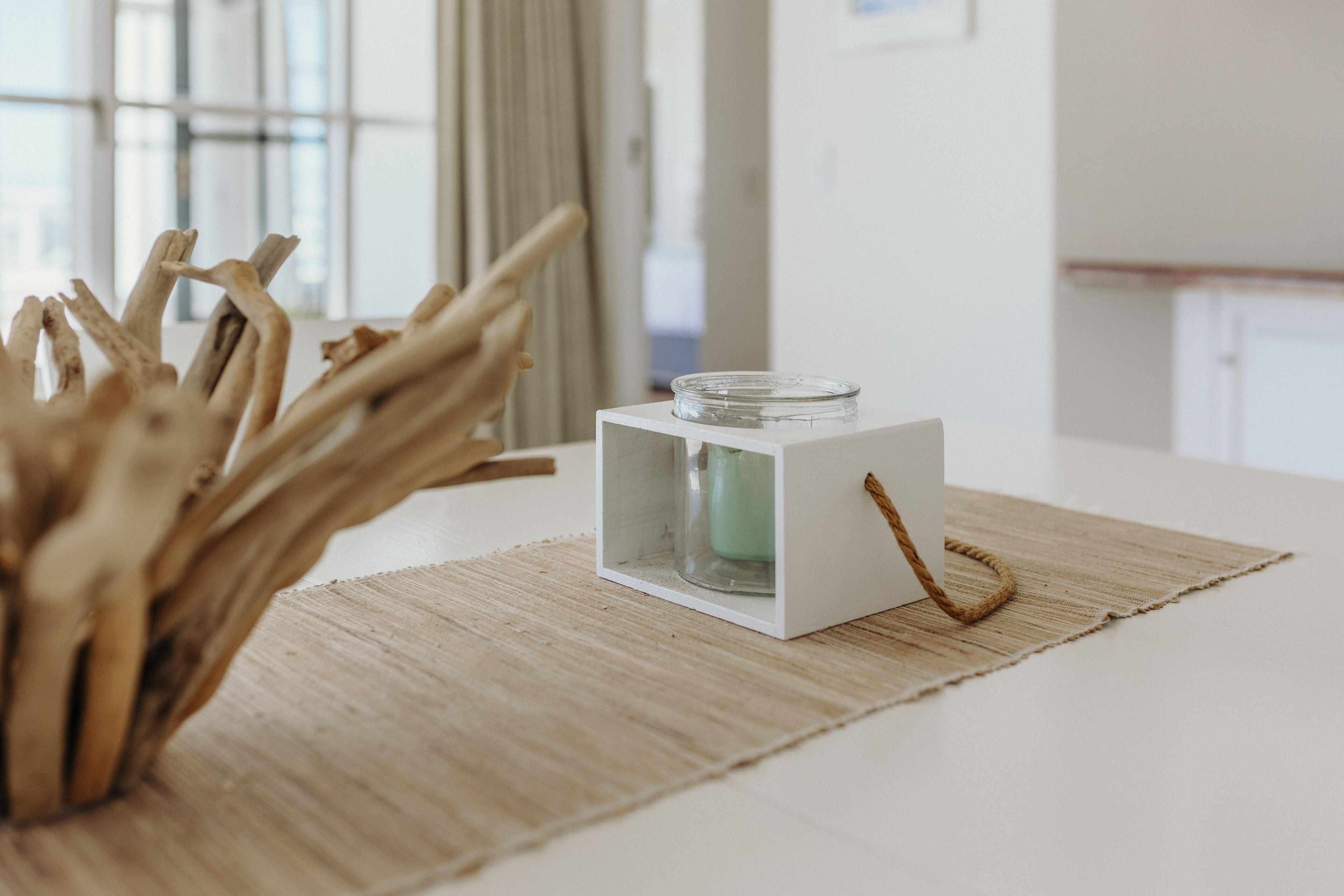A white table with a glass jar candle holder on a woven placemat.