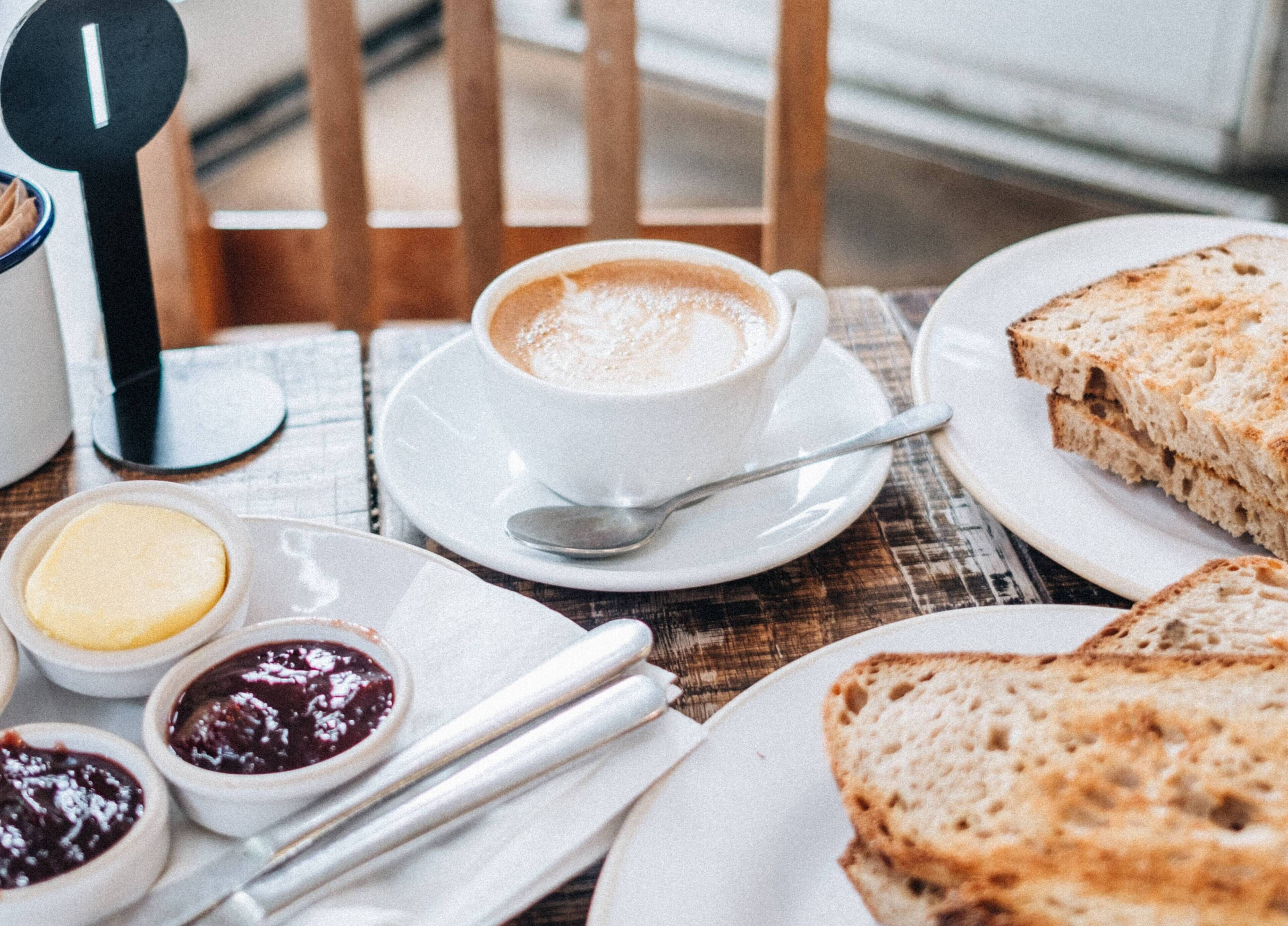 Un tavolo con una tazza di caffè, pane, burro e marmellata.