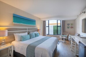 Habitación de hotel con una cama grande, un escritorio y una silla. Se ve follaje verde a través de la ventana.