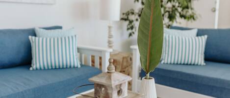 A living room with a blue sofa, striped pillows, a white vase with a green leaf, and a small wooden lantern.