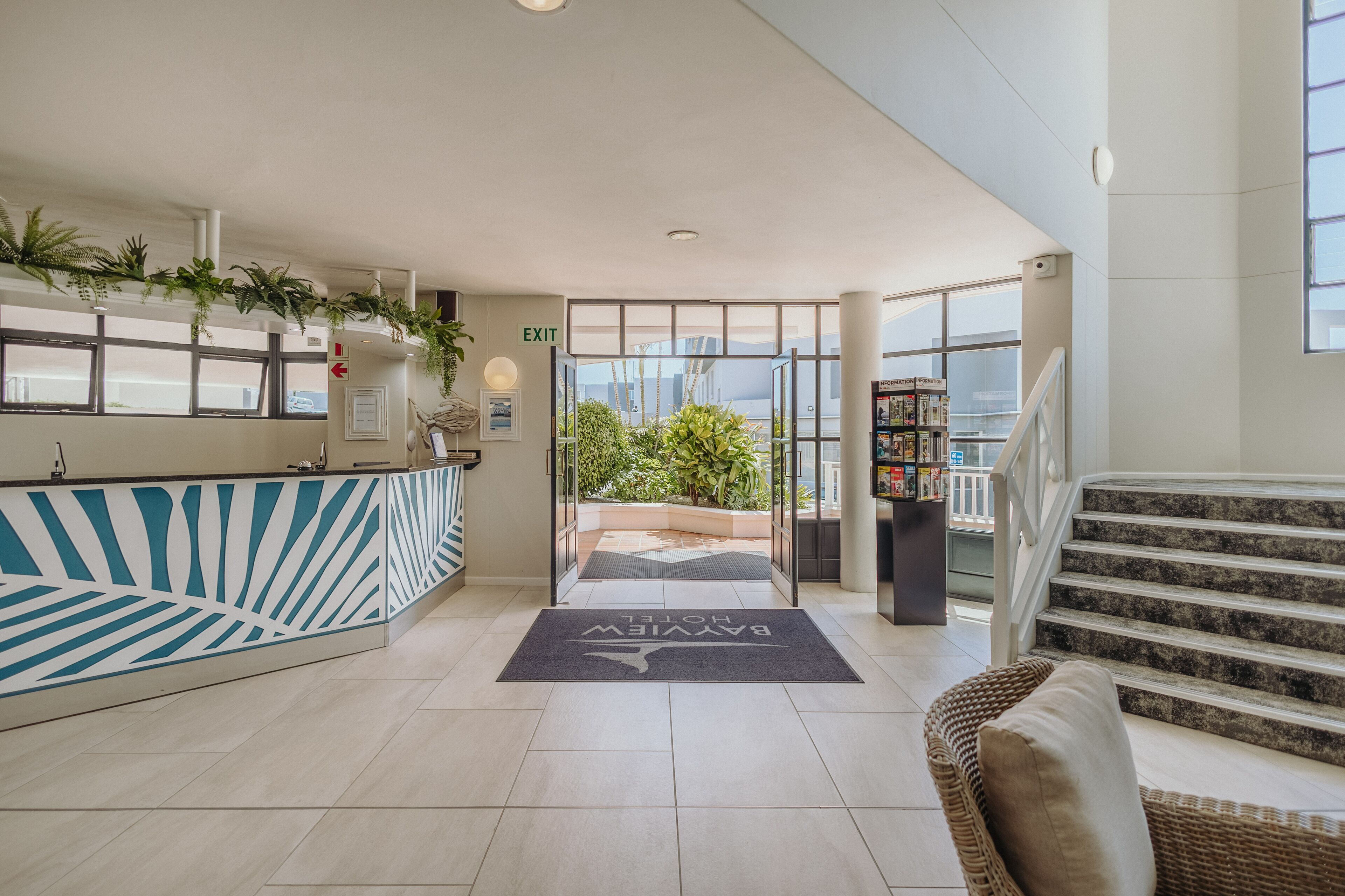 A hotel reception area with a reception desk, a staircase, and a view of the outdoors.