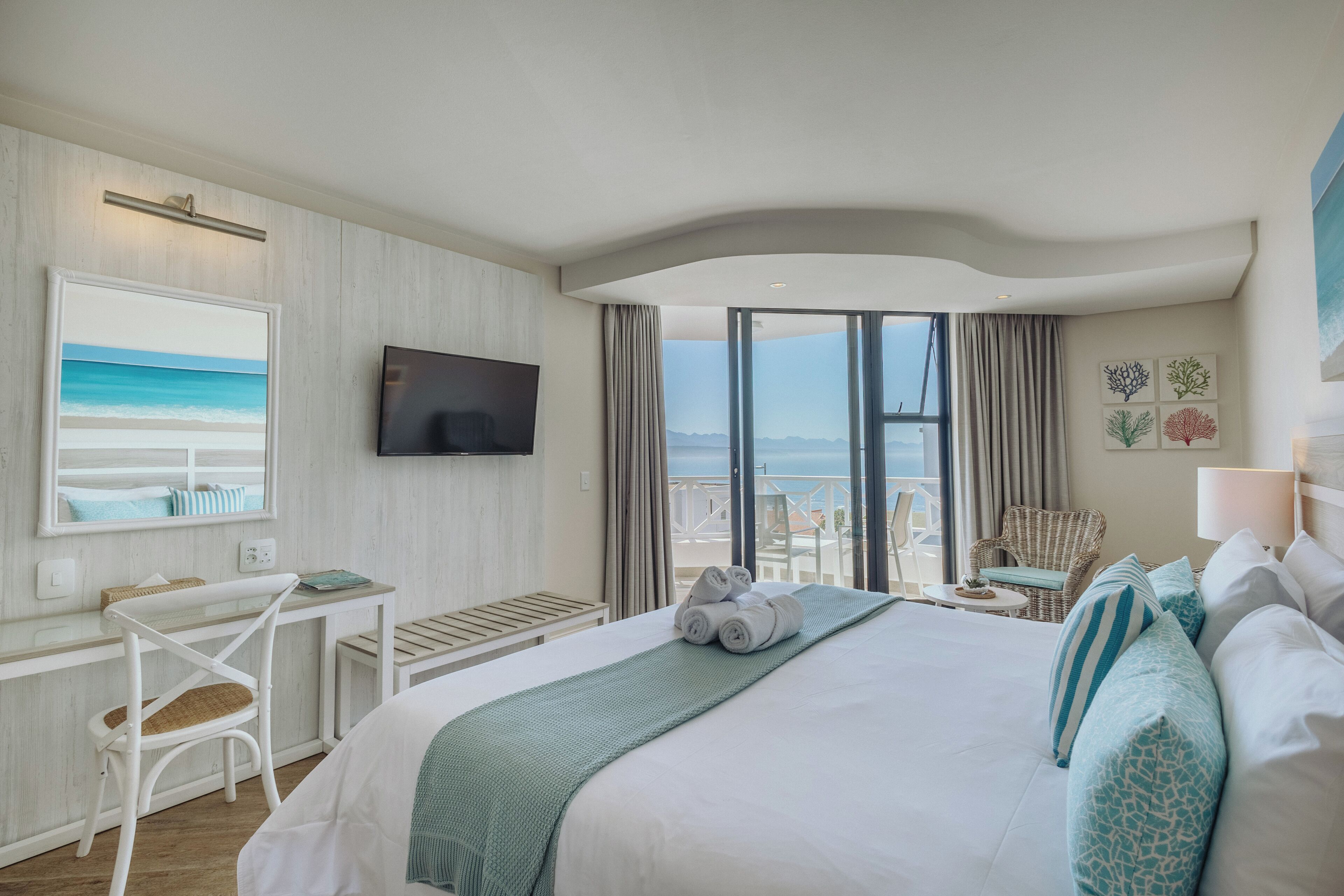 Een hotelkamer met een bed, een bureau, een stoel, een televisietoestel en uitzicht op de oceaan.