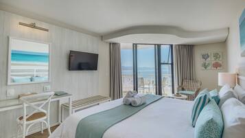 Een hotelkamer met een bed, een bureau, een stoel, een televisietoestel en uitzicht op de oceaan.