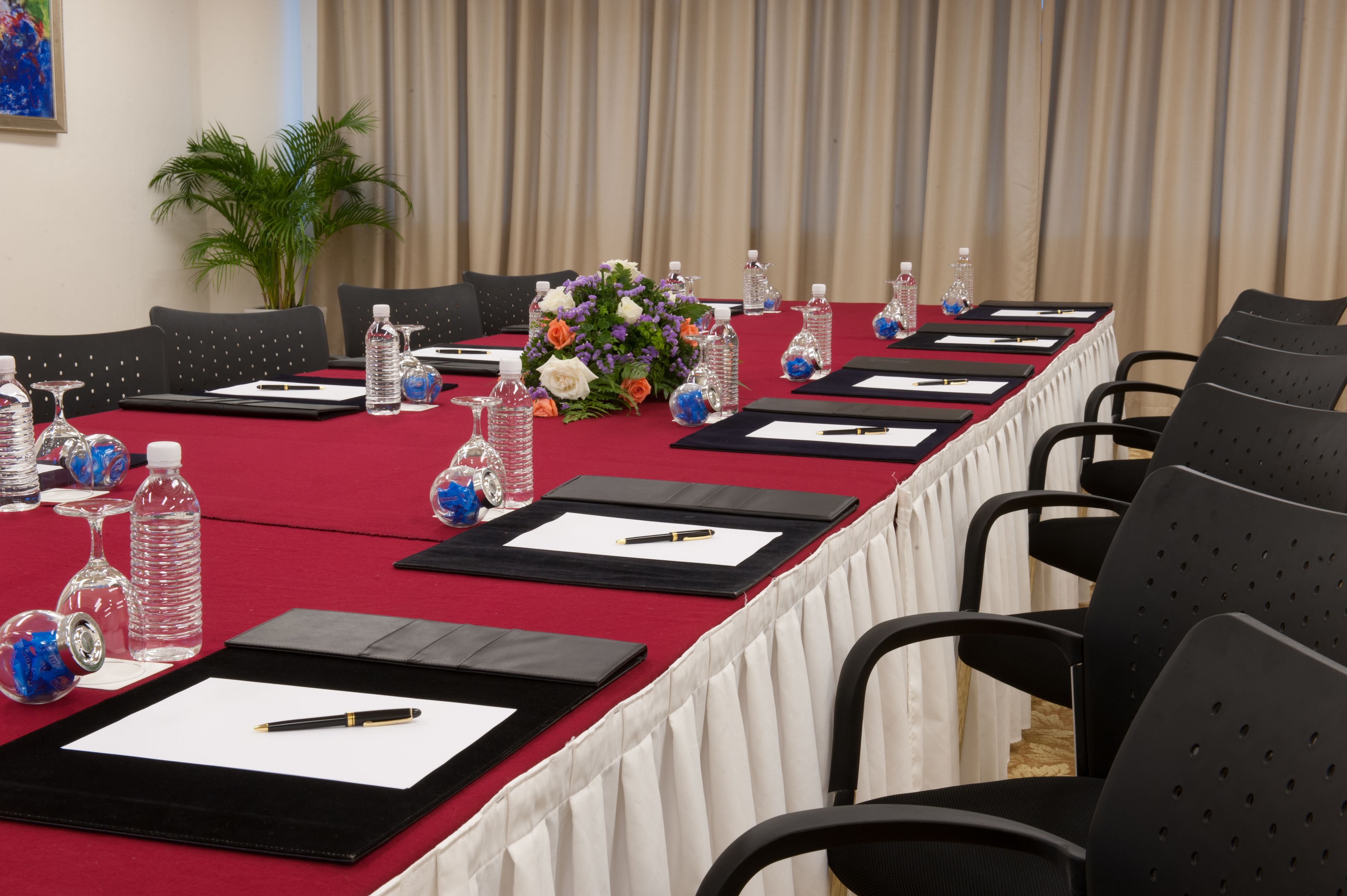 Una sala de conferències amb una taula llarga preparada per a reunions, equipada amb ampolles d'aigua, bolígrafs i fulls de paper.