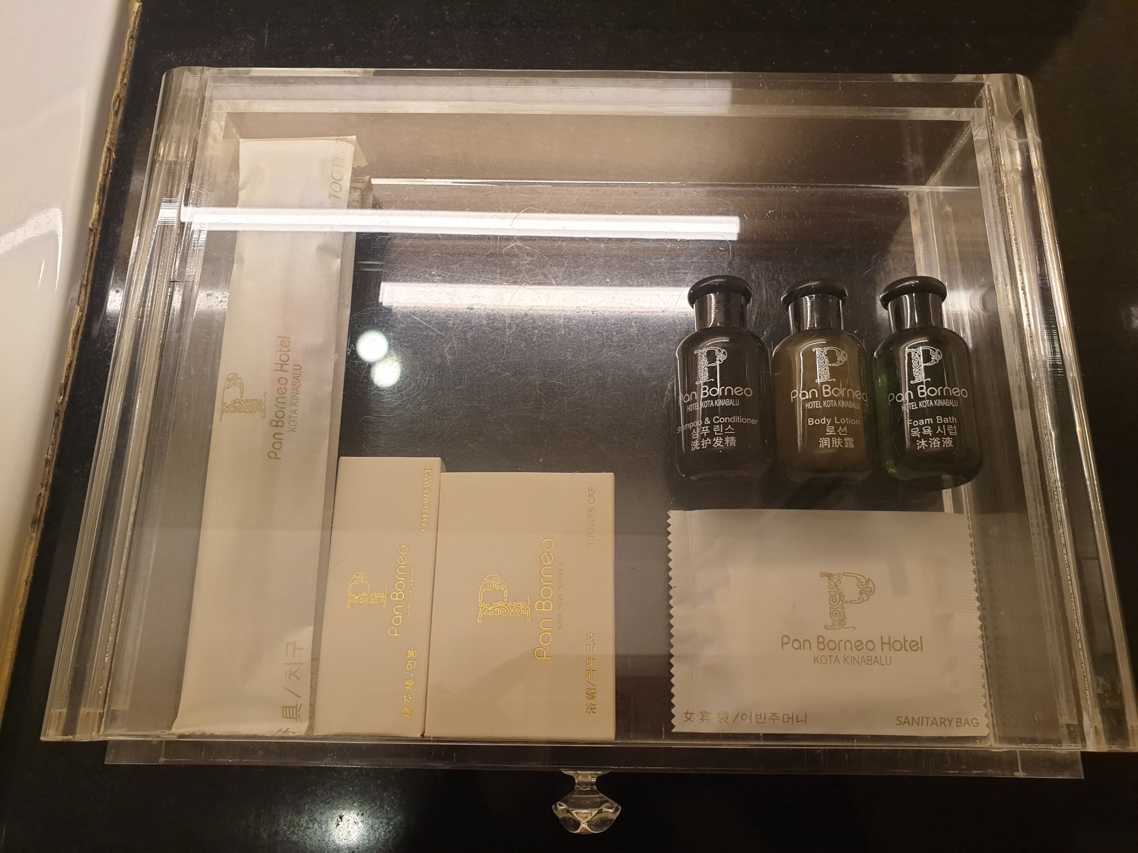 Una vitrina con productos de baño de la marca Pan Borneo Hotel KOTA KINABALU, incluyendo champú, acondicionador, loción corporal y espuma de baño.
