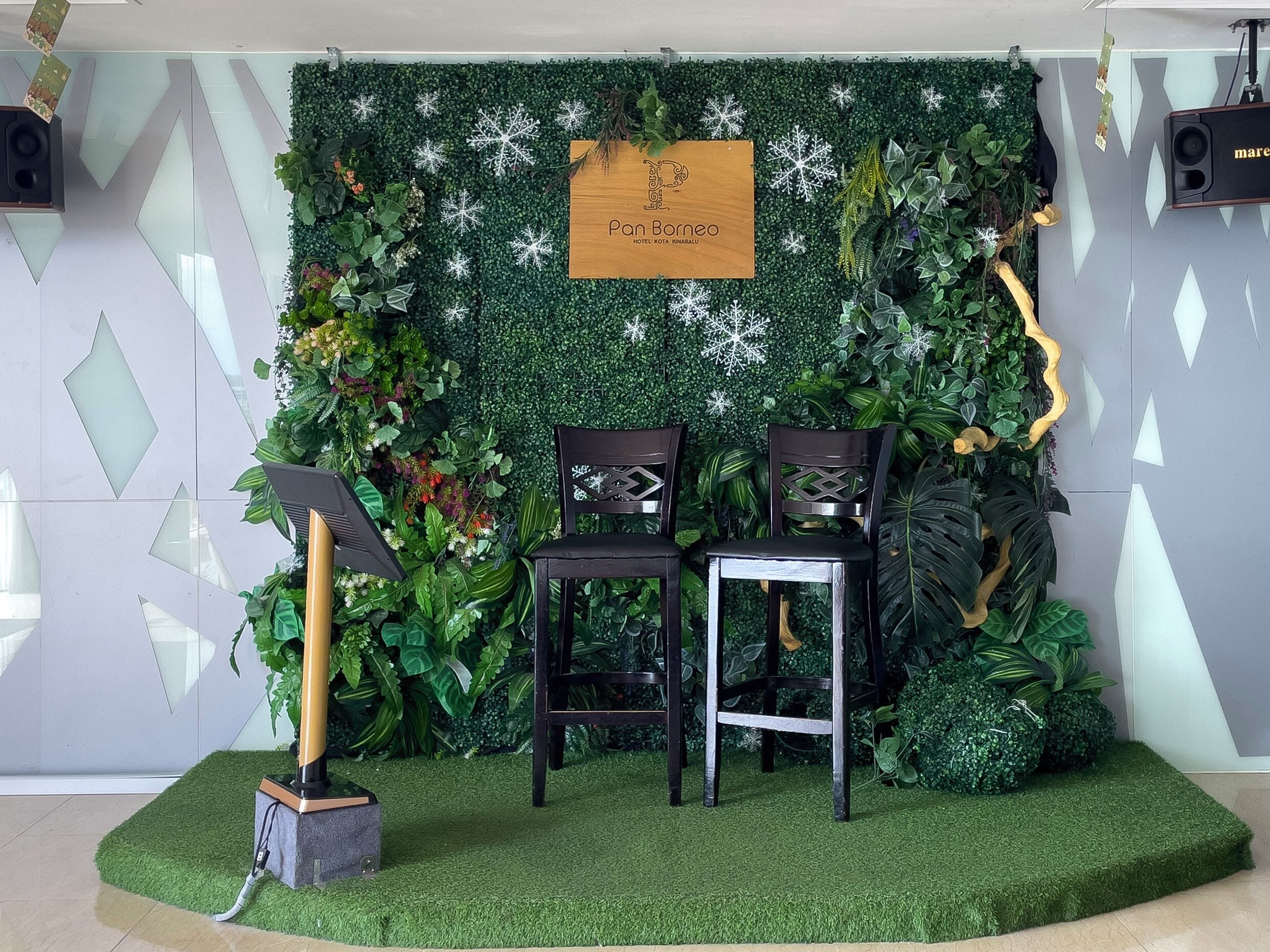 En scene med grøn vegetation og snefnugudsmykning, to træstole og en højttaler til venstre.