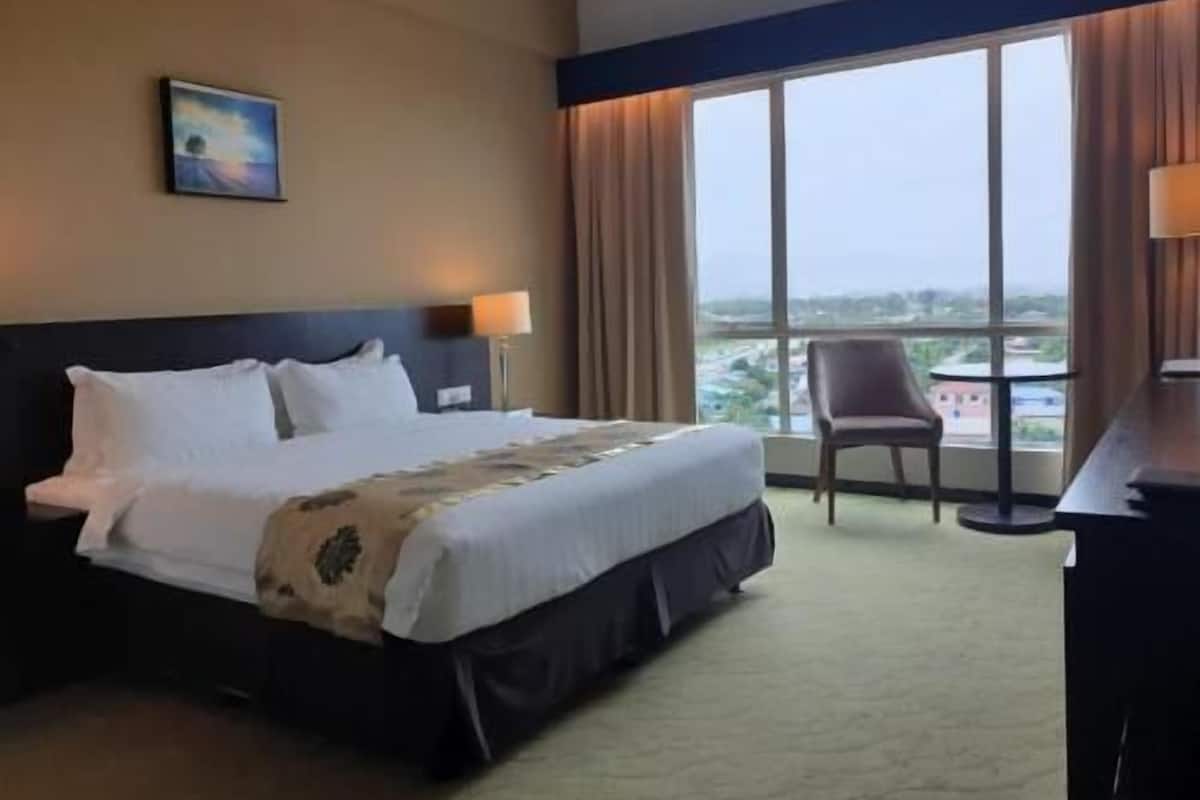 Habitación de hotel con cama, escritorio, silla, ventana con vistas y un cuadro en la pared.