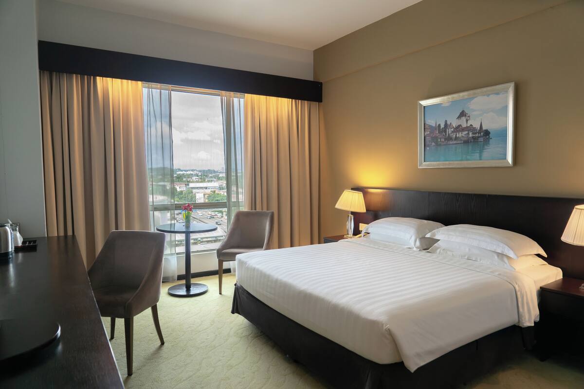 Habitación de hotel con una cama grande, un escritorio, una silla y vistas de la ciudad a través de la ventana.