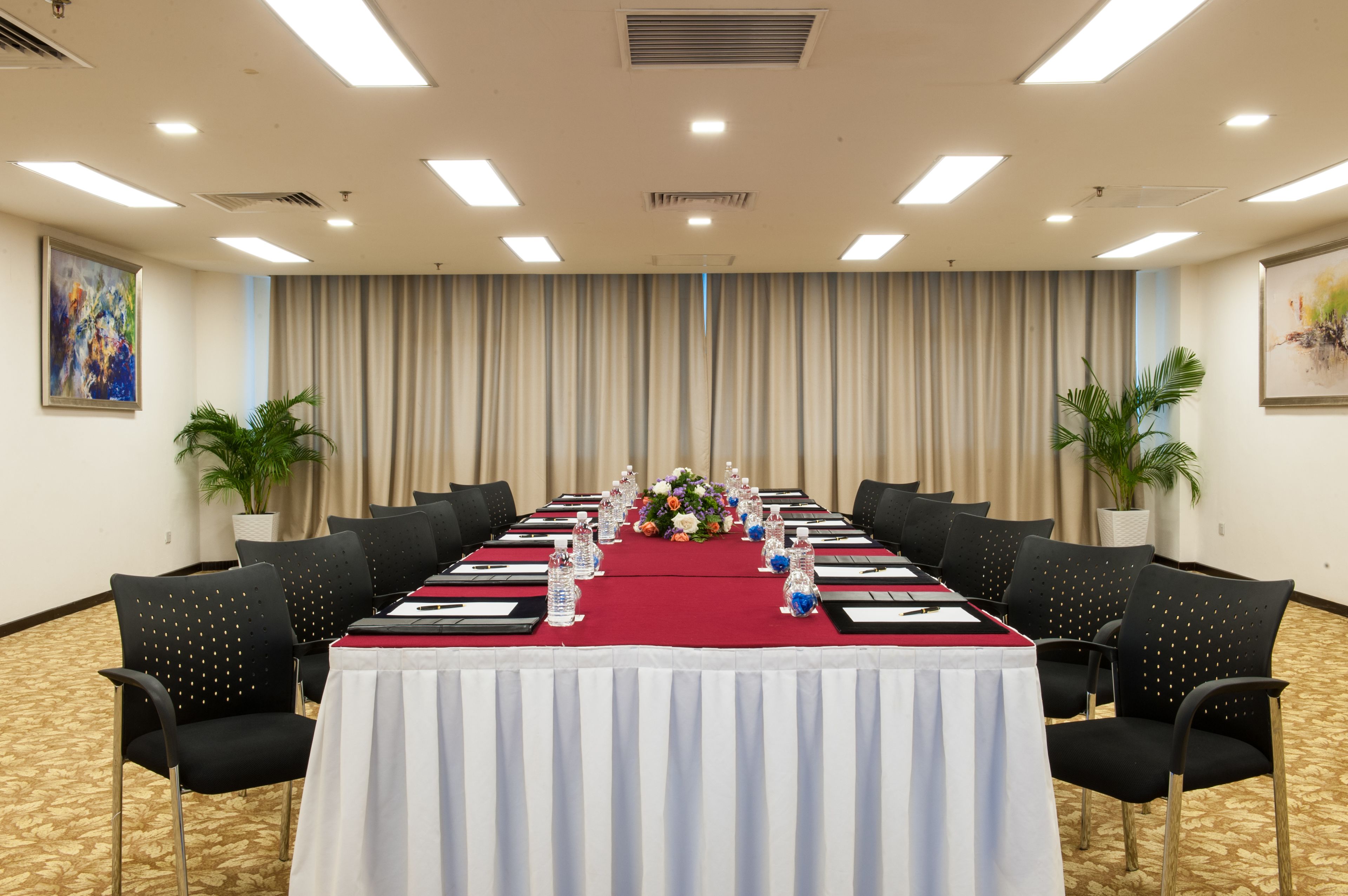 Une salle de conférence avec une longue table, des chaises noires et une nappe rouge. Des plantes en pot sont disposées de part et d’autre de la pièce.