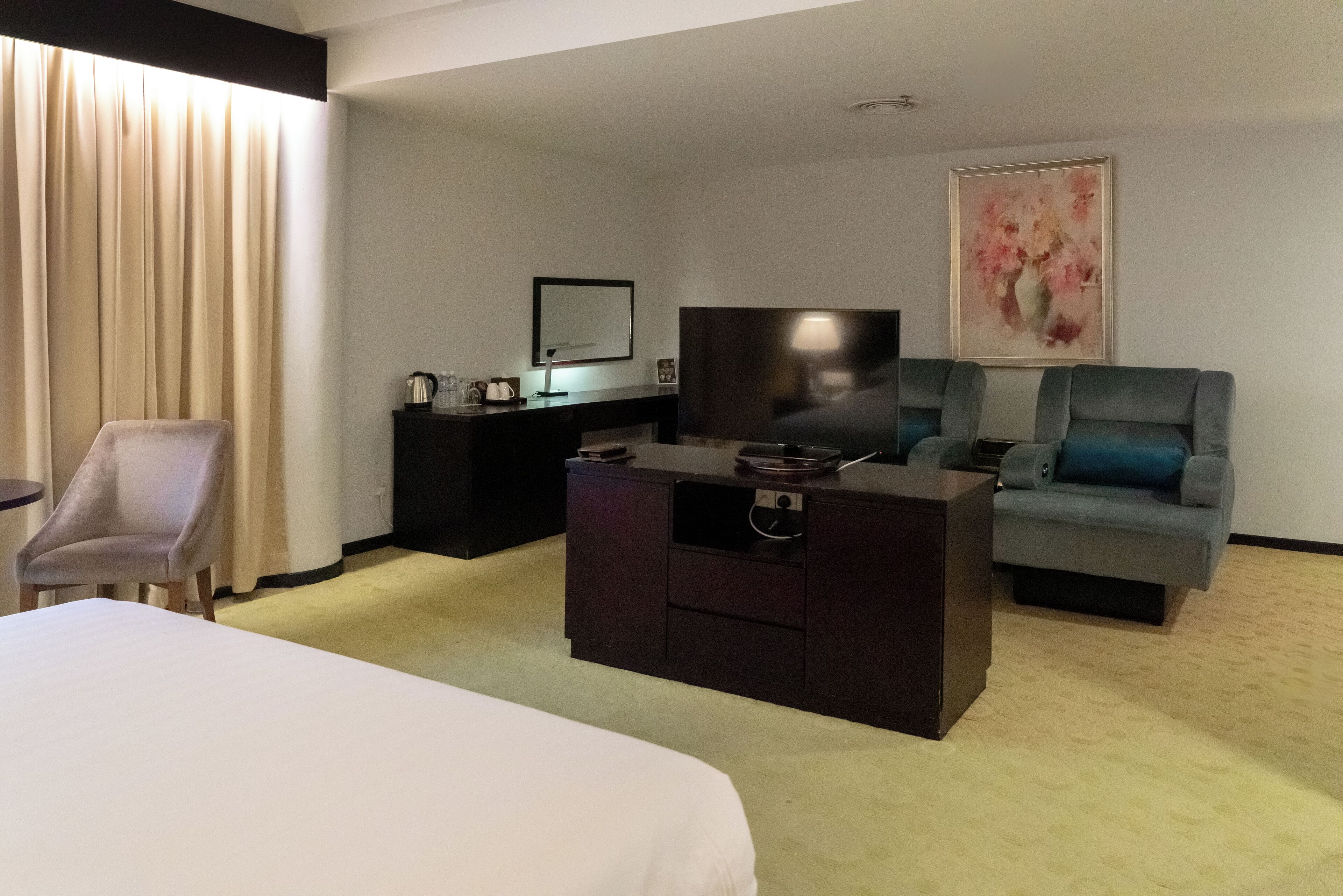 Una habitación de hotel con cama, escritorio con televisor de pantalla plana, sofá, sillón y un cuadro en la pared.