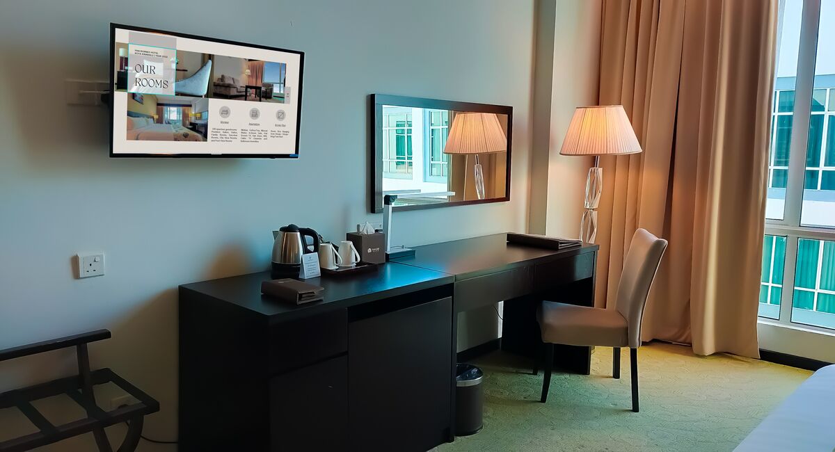 A hotel room with a desk, chair, lamp, and a large window with curtains.