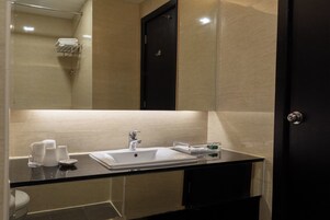 Un baño moderno con cabina de ducha de vidrio, un lavamanos blanco y un mueble oscuro.