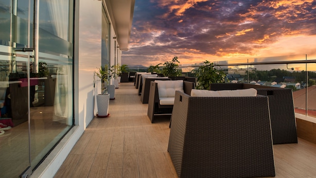 Ein Balkon mit Korbmöbeln und Blumentöpfen mit Blick auf einen Sonnenuntergang mit Wolken.