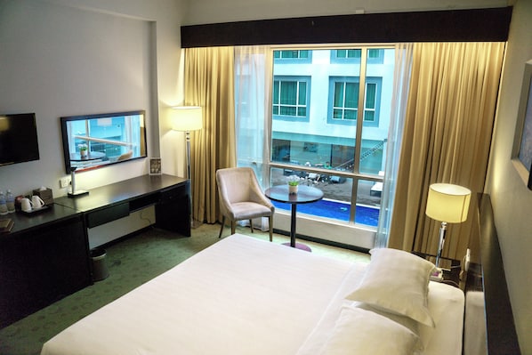 A hotel room with a bed, a desk, a chair, a TV, a window with curtains, and a view of a building. - Pan Borneo Hotel Kota Kinabalu (Kota Kinabalu)