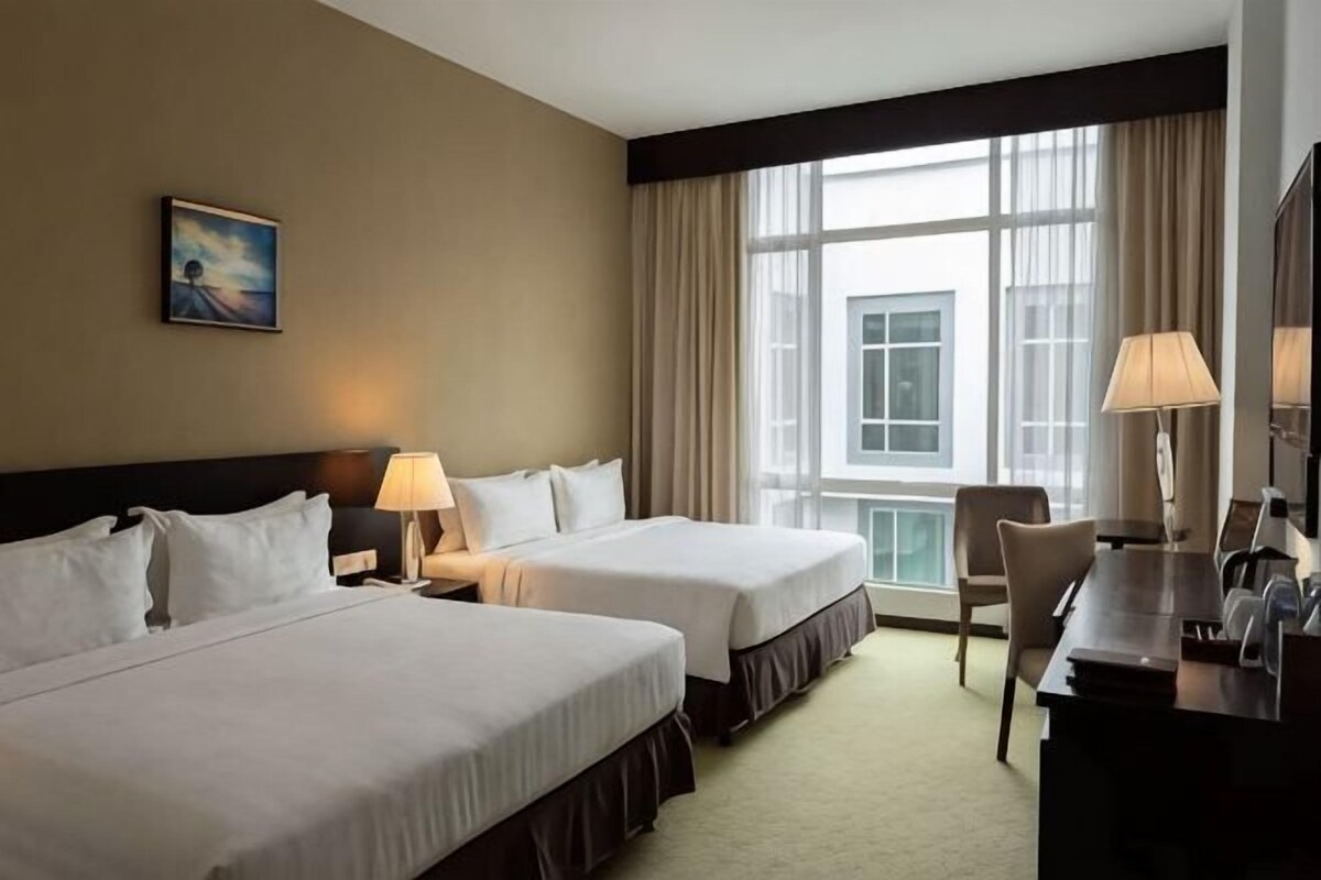 Une chambre d’hôtel avec deux lits, un bureau, une chaise et une grande fenêtre.