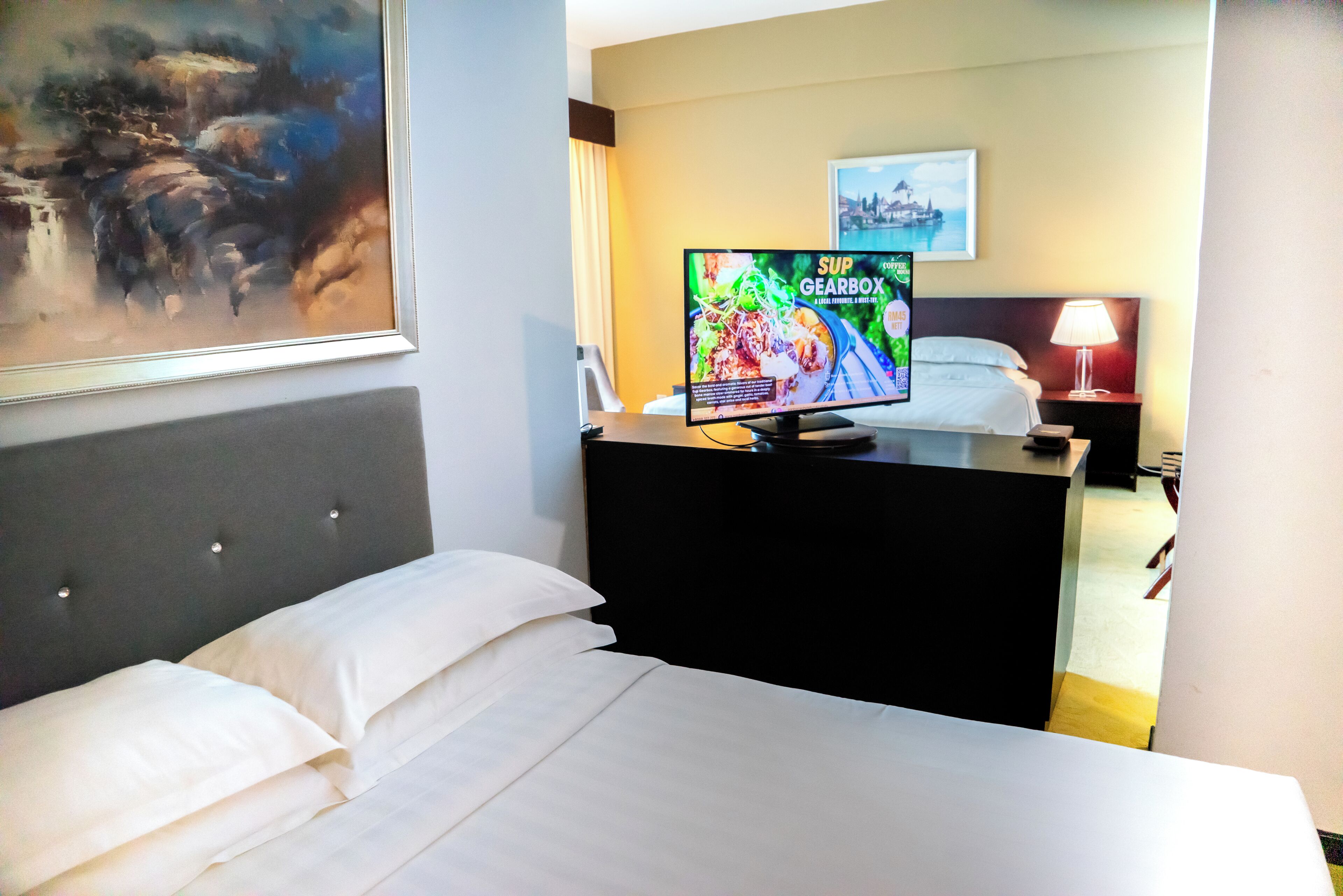 A hotel room with a bed, a TV displaying a game, a painting on the wall, and a lamp on the nightstand.