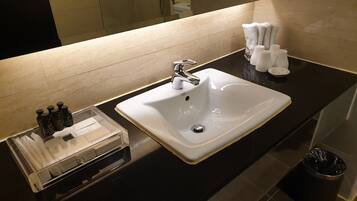 Un lavamanos con un espejo arriba, un dispensador de toallas y un cubo de basura.