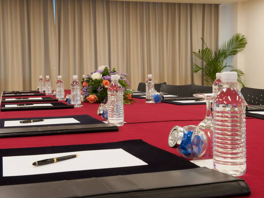 Uma sala de conferência com uma longa mesa preparada para uma reunião, equipada com garrafas de água, canetas e cadernos.