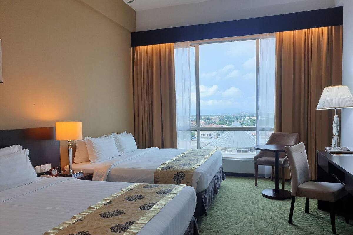 Habitación de hotel con dos camas, un escritorio, una silla y un ventanal con vistas a la ciudad.