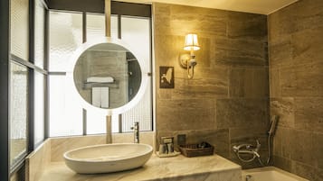 A bathroom with a large oval sink, a round mirror, a wall-mounted light fixture, and a shower area.