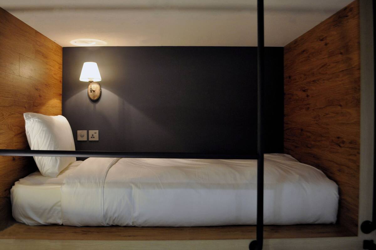 A bunk bed with a headboard, a wall-mounted lamp, and a wooden panel wall.