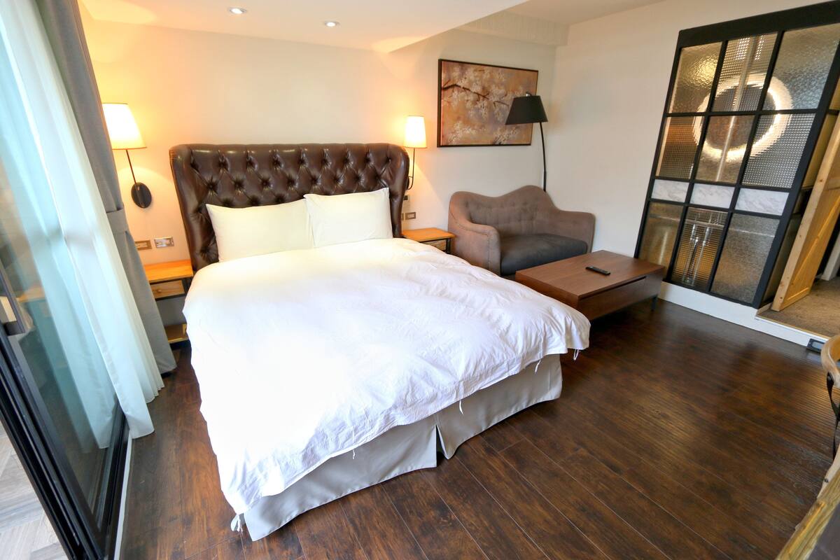 A hotel room with a large bed, a sofa, a small table, and a sliding glass door.